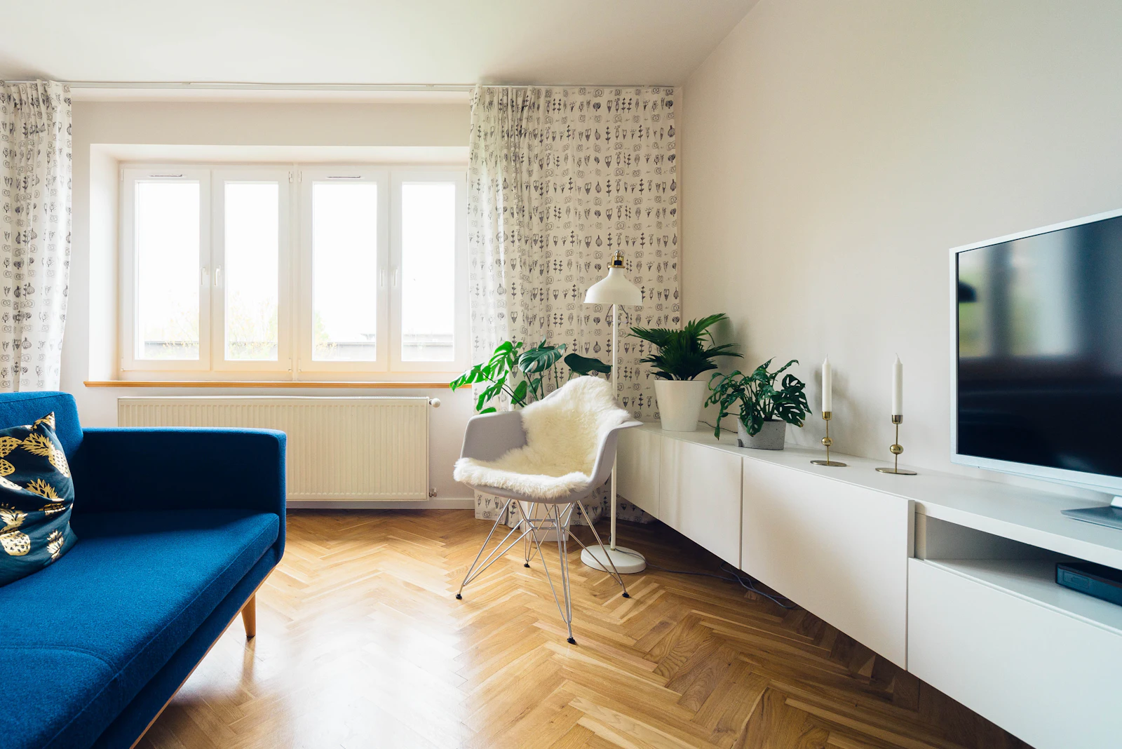 Una sala con piso de espiga y un sofá azul bajo ventanas altas. Fotografía ilustrativa.